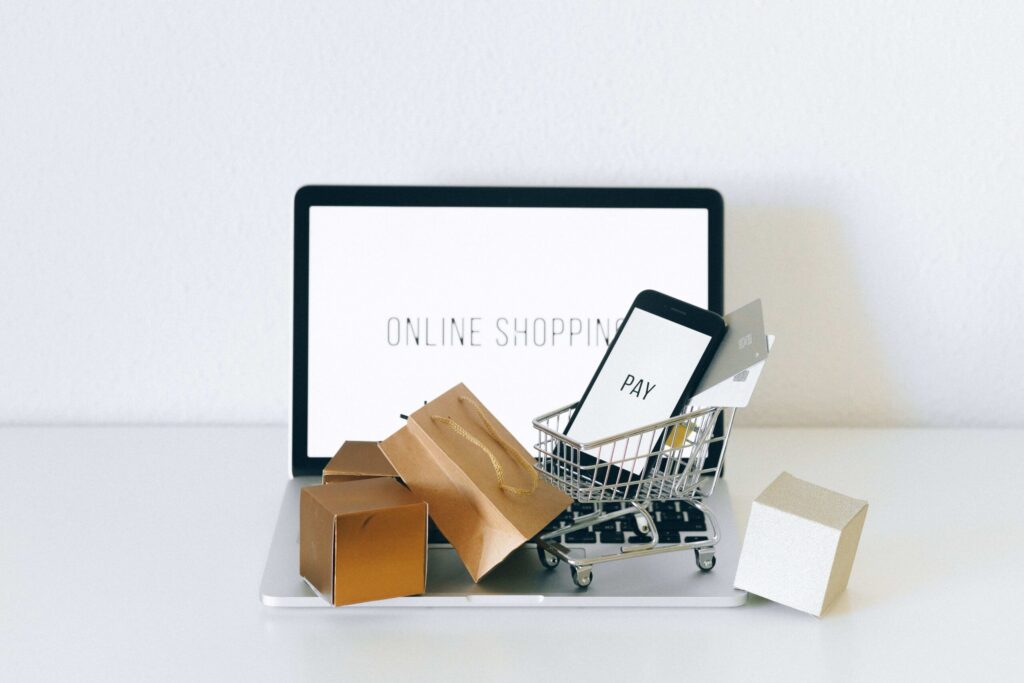 Onlineshop erstellen lassen – Laptop mit Warenkorb, Smartphone und Paketen als Symbol für Online-Shopping