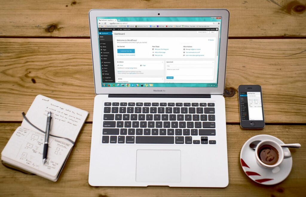 WordPress Dashboard auf einem Laptop mit Notizbuch und Kaffee auf einem Holztisch